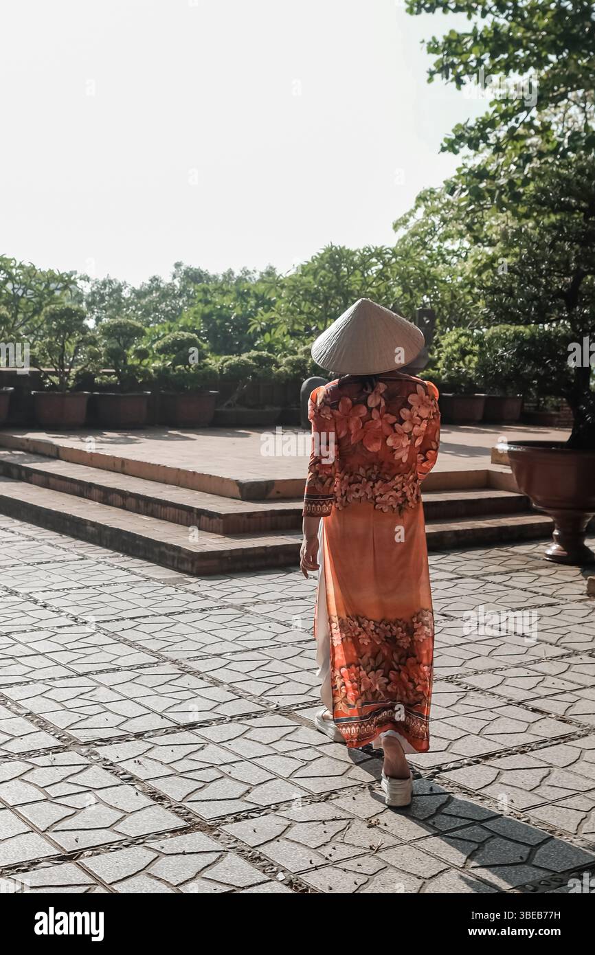 Dame vietnamienne avec la robe traditionnelle Ao Dai Vietnam. Vue arrière de belle femme asiatique voyageur en robe traditionnelle et chapeau conique dans un jardin Banque D'Images