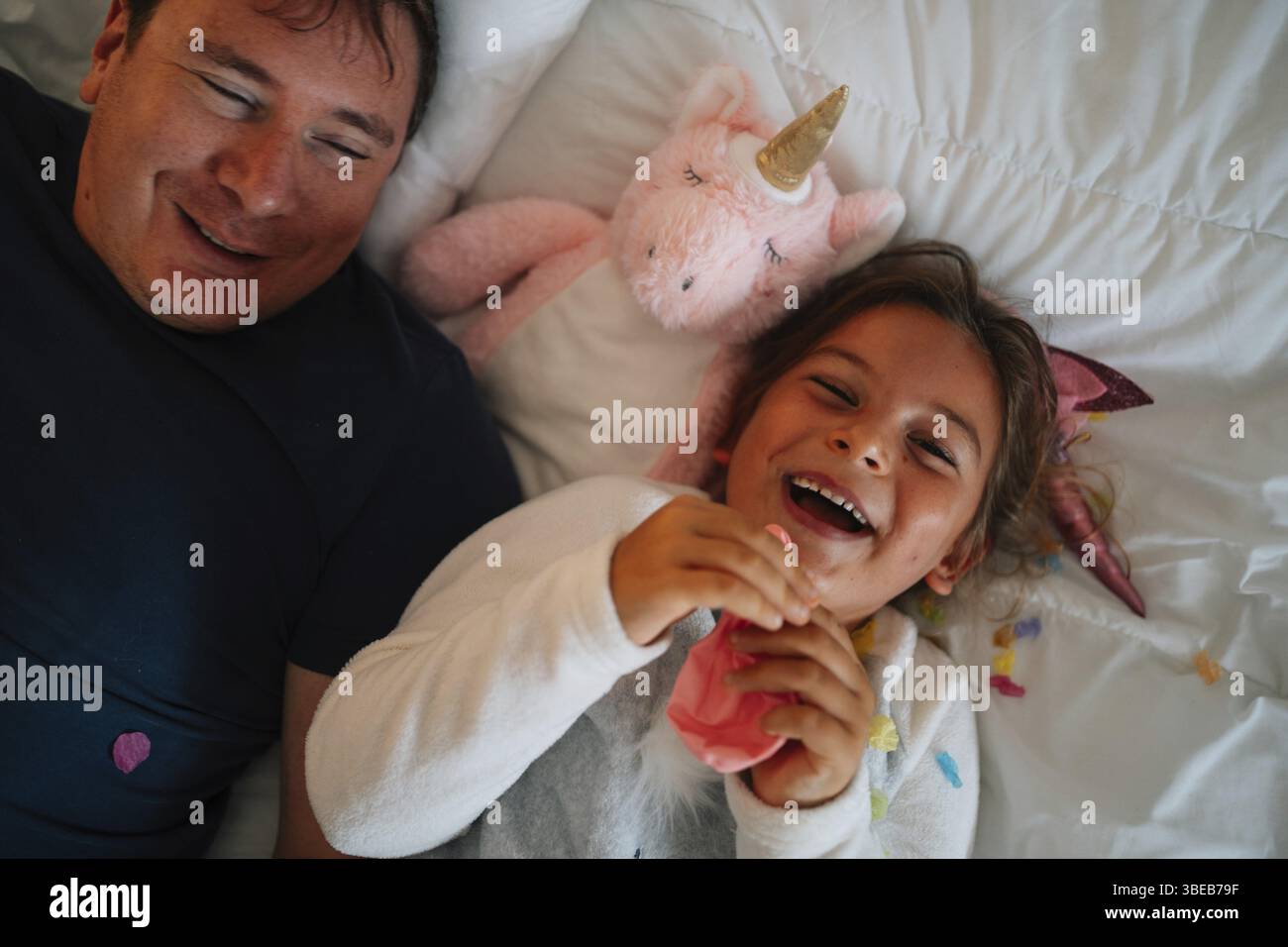 Joyeux homme adulte caucasien et enfant riant avec jouet licorne sur le lit Banque D'Images