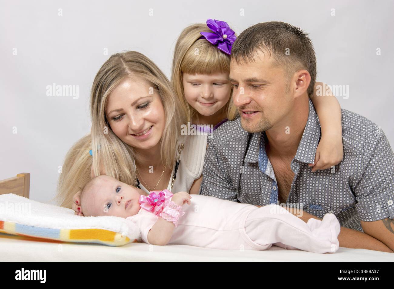 Les jeunes parents et la fille s'asseoir à la crèche, la crèche est sur deux mois d'un bébé sur son dos Banque D'Images