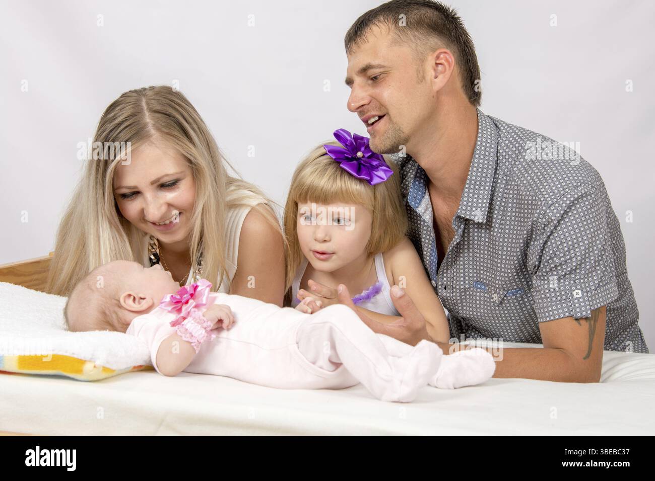 Les jeunes parents et la fille s'asseoir à la crèche, la crèche est sur deux mois d'un bébé sur son dos Banque D'Images
