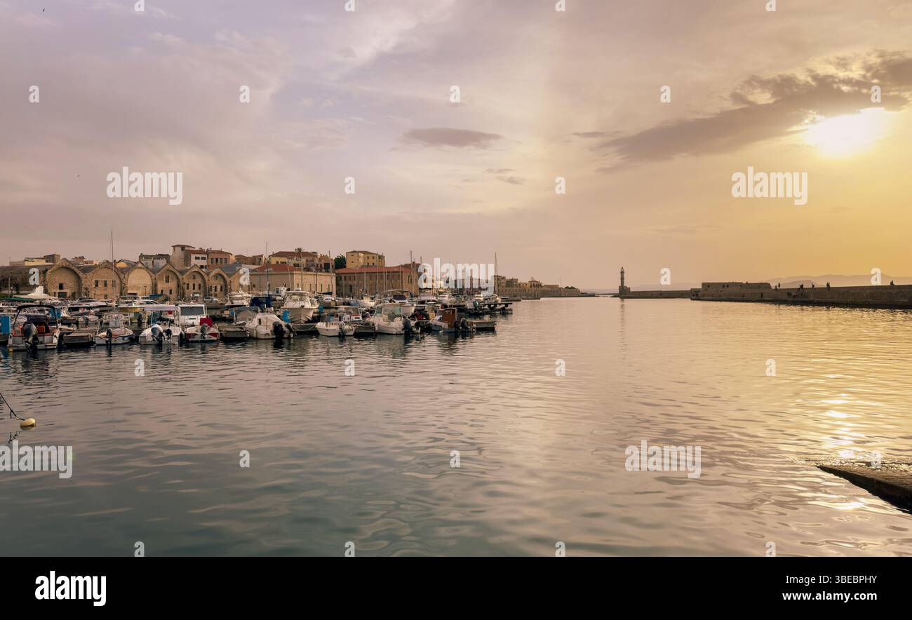 Crète, vieux port de Chania. Bâtiments riverains au coucher du soleil, vieux phare, chantiers navals et marina, ciel nuageux Banque D'Images