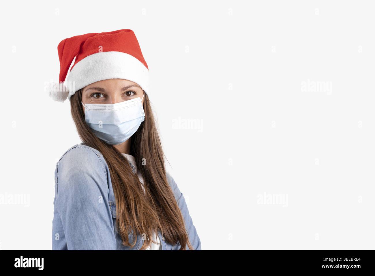 Jeune femme avec masque médical et chapeau de père noël sur fond blanc. Noël en quarantaine. Banque D'Images