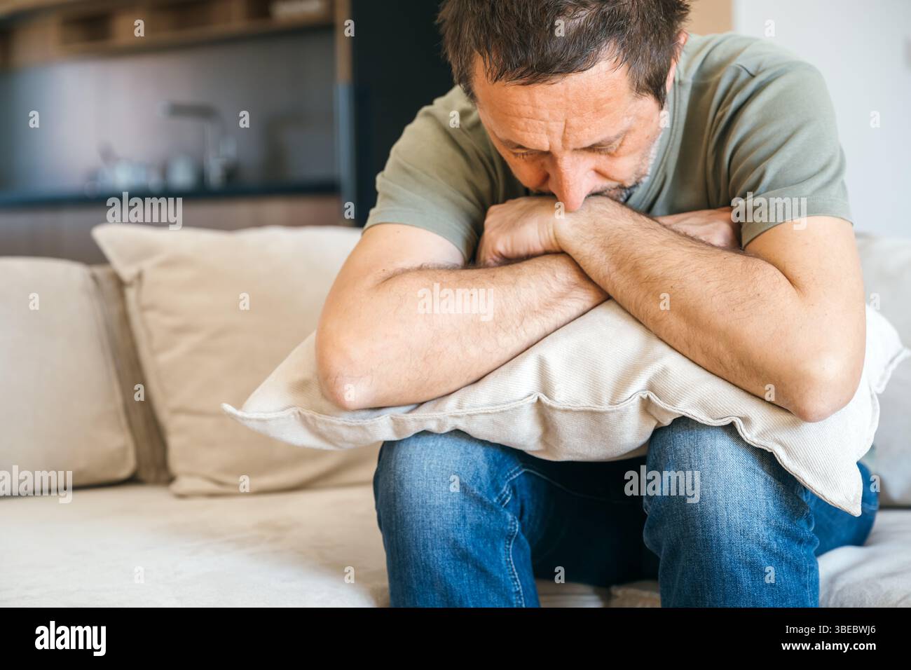 Homme triste désespéré assis dans le canapé et l'oreiller serrant, se sentant misérable et déprimé, la mise au point sélective Banque D'Images