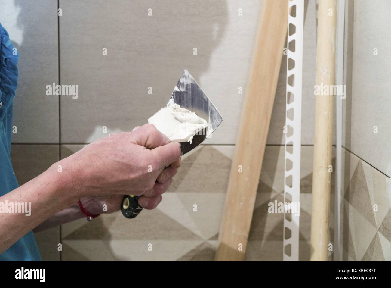Travailleur avec une spatule en caoutchouc remplir les coutures avec une solution. Travaux de finition, mise au point floue. La technologie de pose de carreaux Banque D'Images