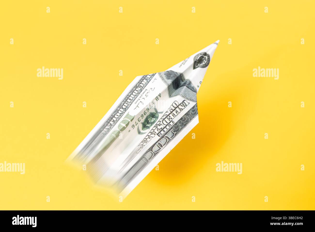 Un billet de cent dollars plié comme un avion de papier volant rapidement sur un fond jaune représentant la puissance économique et la croissance Banque D'Images