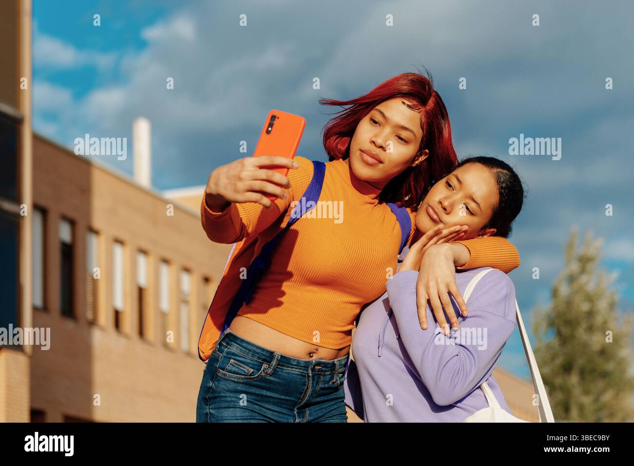 Deux jeunes femmes latines, l'une avec les cheveux roux et l'autre avec les cheveux noirs, sont vues profiter d'une journée ensoleillée sur un campus universitaire tout en prenant un selfie avec un s. Banque D'Images