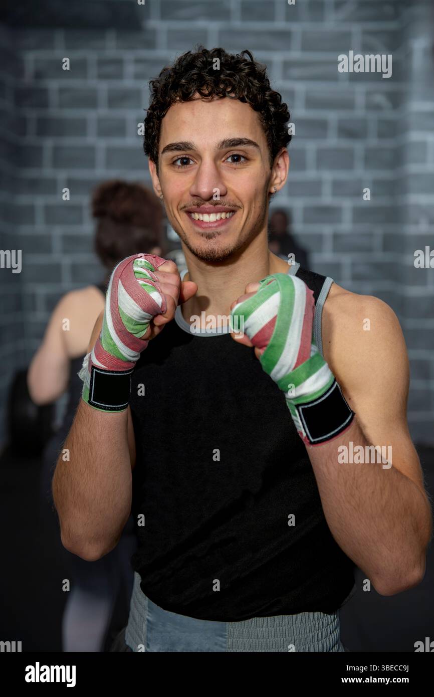 Jeune boxeur souriant tout en affichant des mains bandées pendant l'entraînement dans un gymnase, incarnant la force et le dévouement dans sa routine d'entraînement Banque D'Images