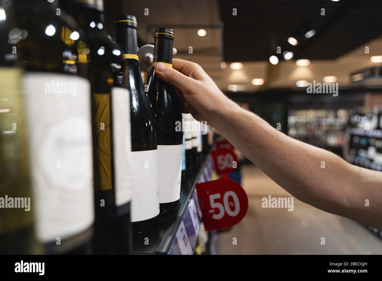Une personne sélectionne une bouteille de vin dans une étagère de supermarché, en mettant l'accent sur sa main et les bouteilles de vin. concept de consommateur masculin . Banque D'Images