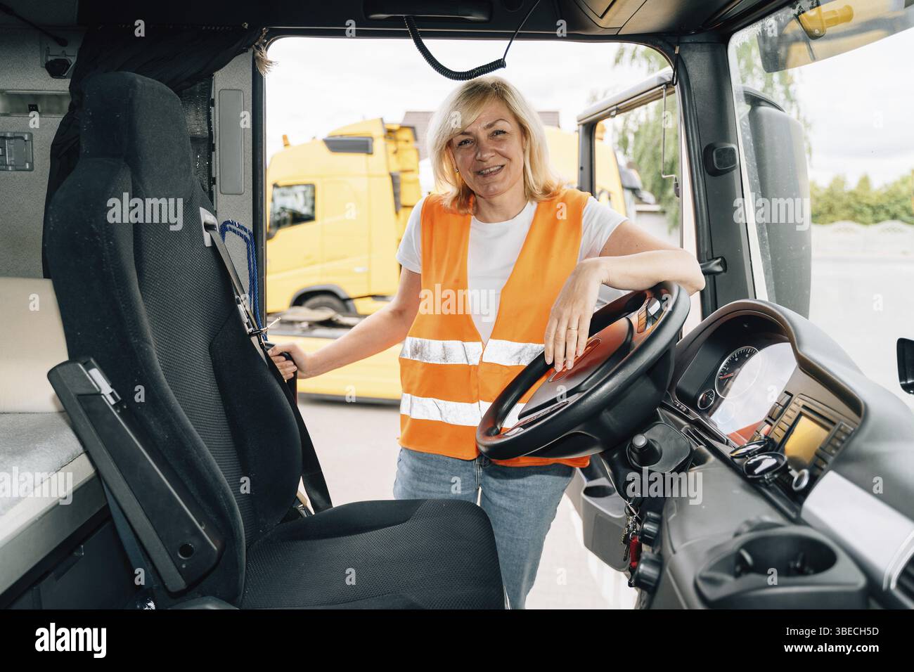 Volant de direction de conducteur de camion de femme mature à l'intérieur de la cabine de camion. Portrait de camionneur féminin d'âge moyen heureux. Banque D'Images