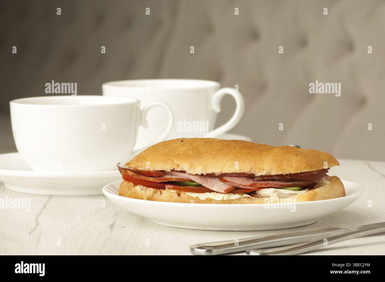 Sandwich et deux tasses de café sur une table avec couverts Banque D'Images
