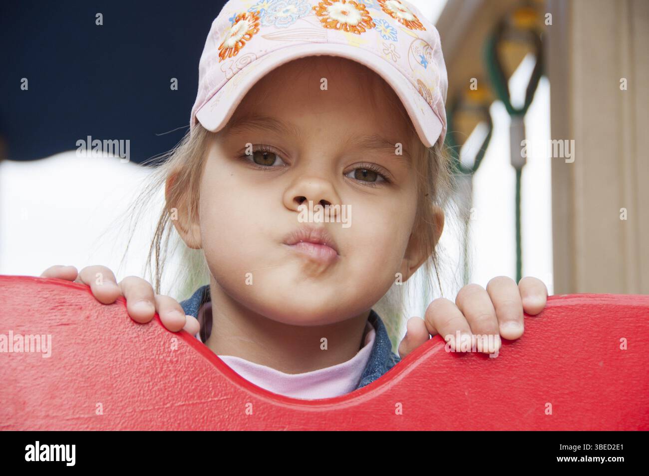 Une fille jette un coup d'œil par le haut du bouclier, alors qu'elle est sur le terrain de jeu. La fille porte une casquette Banque D'Images