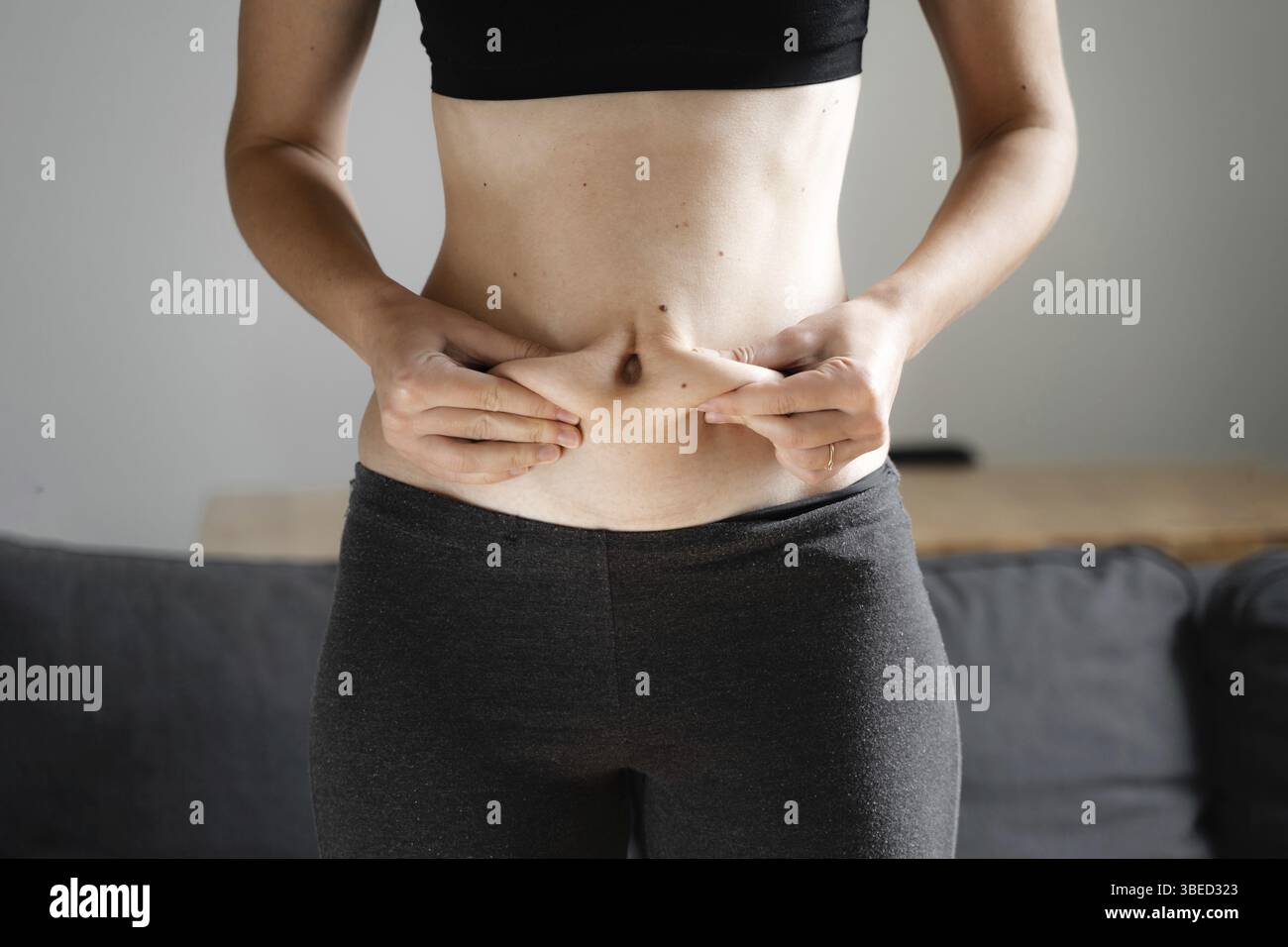 Jeune femme à la maison tenant la graisse du ventre avec les mains.Concept de neutralité du corps.Accepter le corps et le poids.Mauvaise alimentation de carb. Banque D'Images