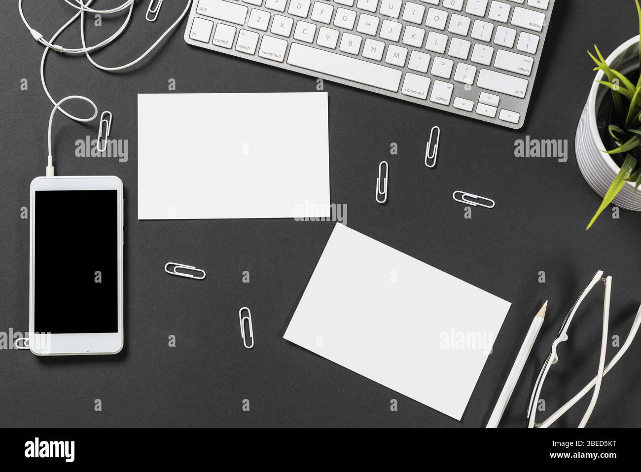 Vue de dessus du lieu de travail moderne avec clavier d'ordinateur. Surface noire plate avec smartphone et papier blanc vierge. Vue de dessus de l'espace de travail de bureau à domicile. DIG Banque D'Images
