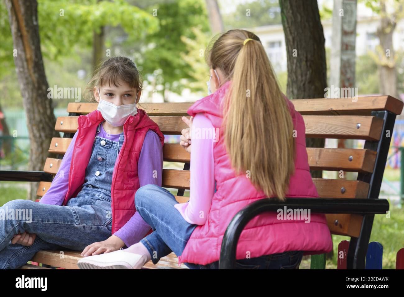 Les amies avec masque de visage parlent tout en étant assis sur un banc dans l'aire de jeux Banque D'Images