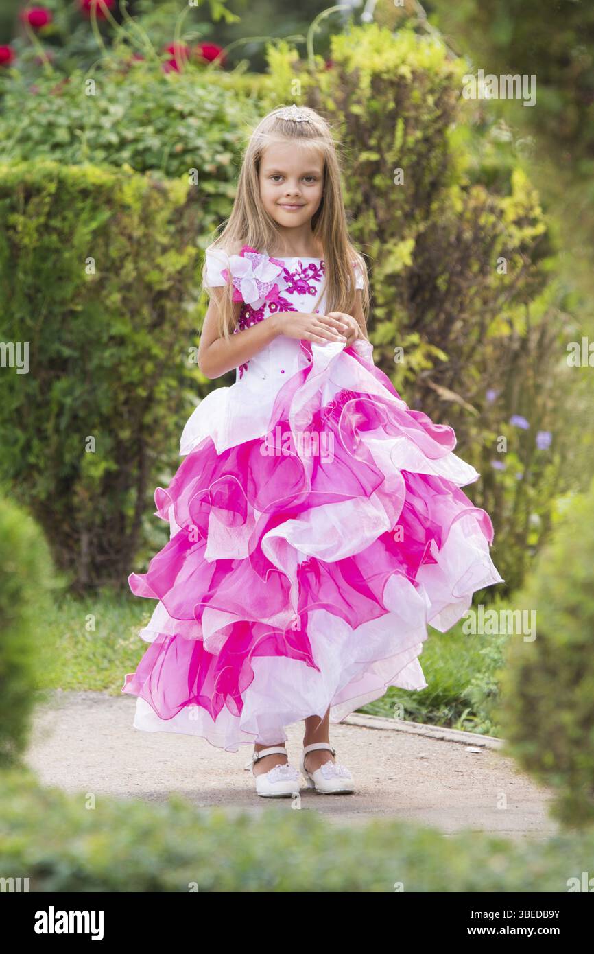 Heureux fillette de six ans dans un cadre de soirée robe rose marche à travers le jardin vert Banque D'Images