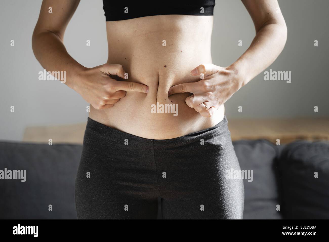 Jeune femme à la maison tenant la graisse du ventre avec les mains.Concept de neutralité du corps.Accepter le corps et le poids.Mauvaise alimentation de carb. Banque D'Images