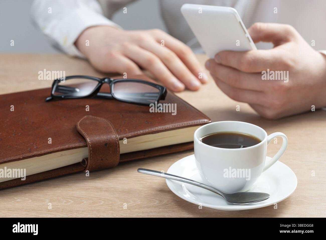 Homme en chemise blanche à l'aide d'un smartphone comme assis au bureau avec une tasse de café. Application professionnelle et technologie mobile. Navigation Internet et communication Banque D'Images