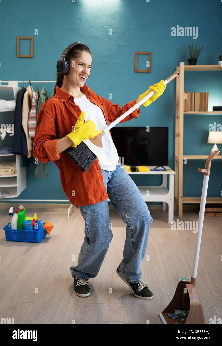 joyeuse jeune femme faisant des travaux ménagers pour jouer à la guitare dans le salon à la maison dansant en s'amusant. Concept de nettoyage et de ménage Banque D'Images