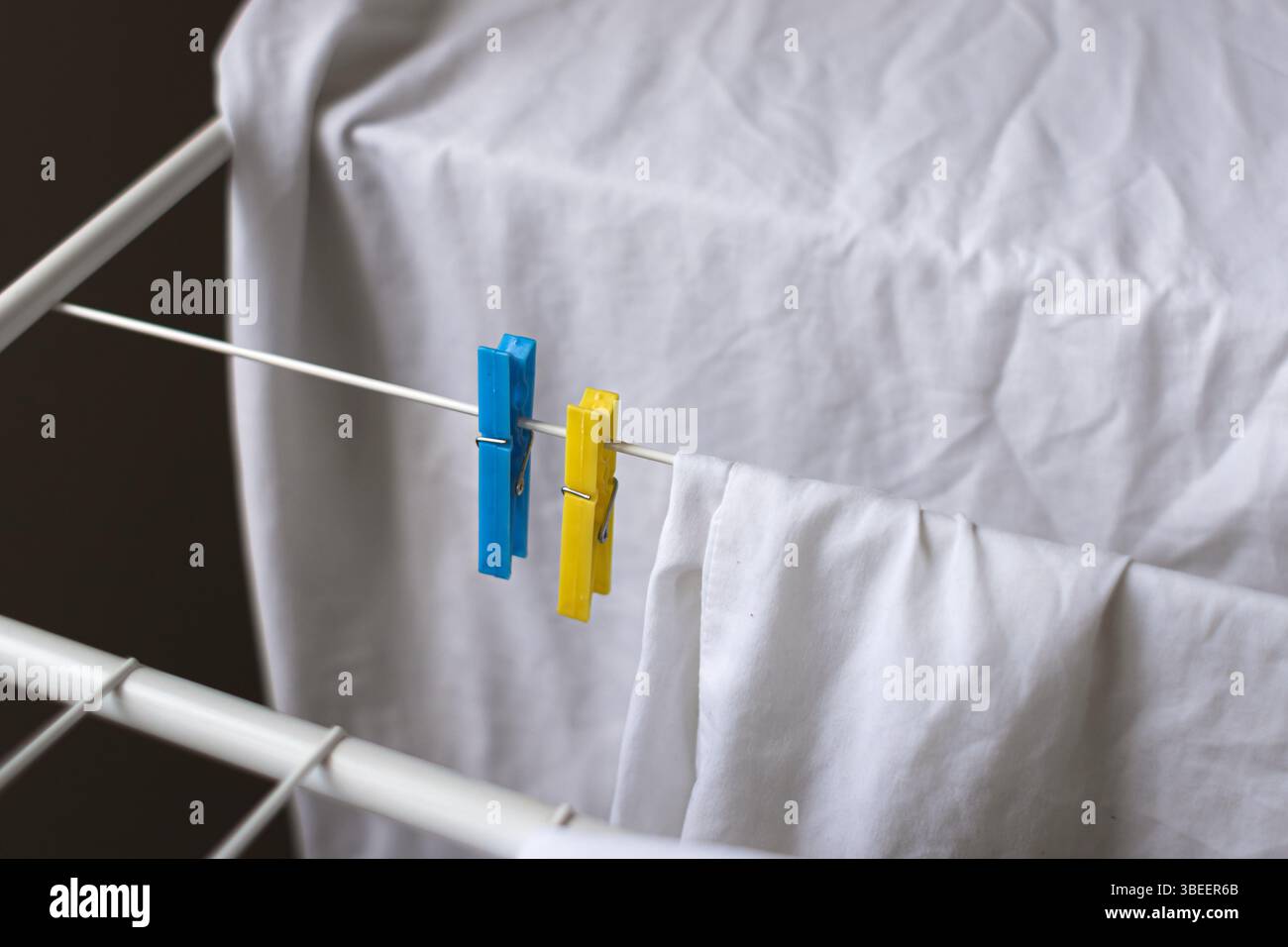 Les vêtements blancs lavés sèchent à côté des pinces à linge bleues et jaunes. Couleur blanche. Pinces à linge sur le sèche-linge. Les choses sèchent après le lavage. Odeur fraîche. Banque D'Images