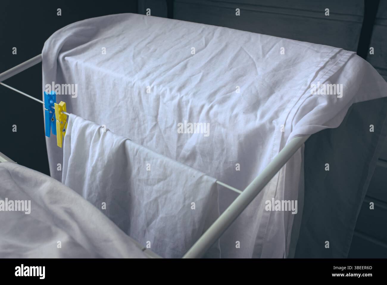 Les vêtements blancs lavés sèchent à côté des pinces à linge bleues et jaunes. Couleur blanche. Pinces à linge sur le sèche-linge. Les choses sèchent après le lavage. Odeur fraîche. Banque D'Images