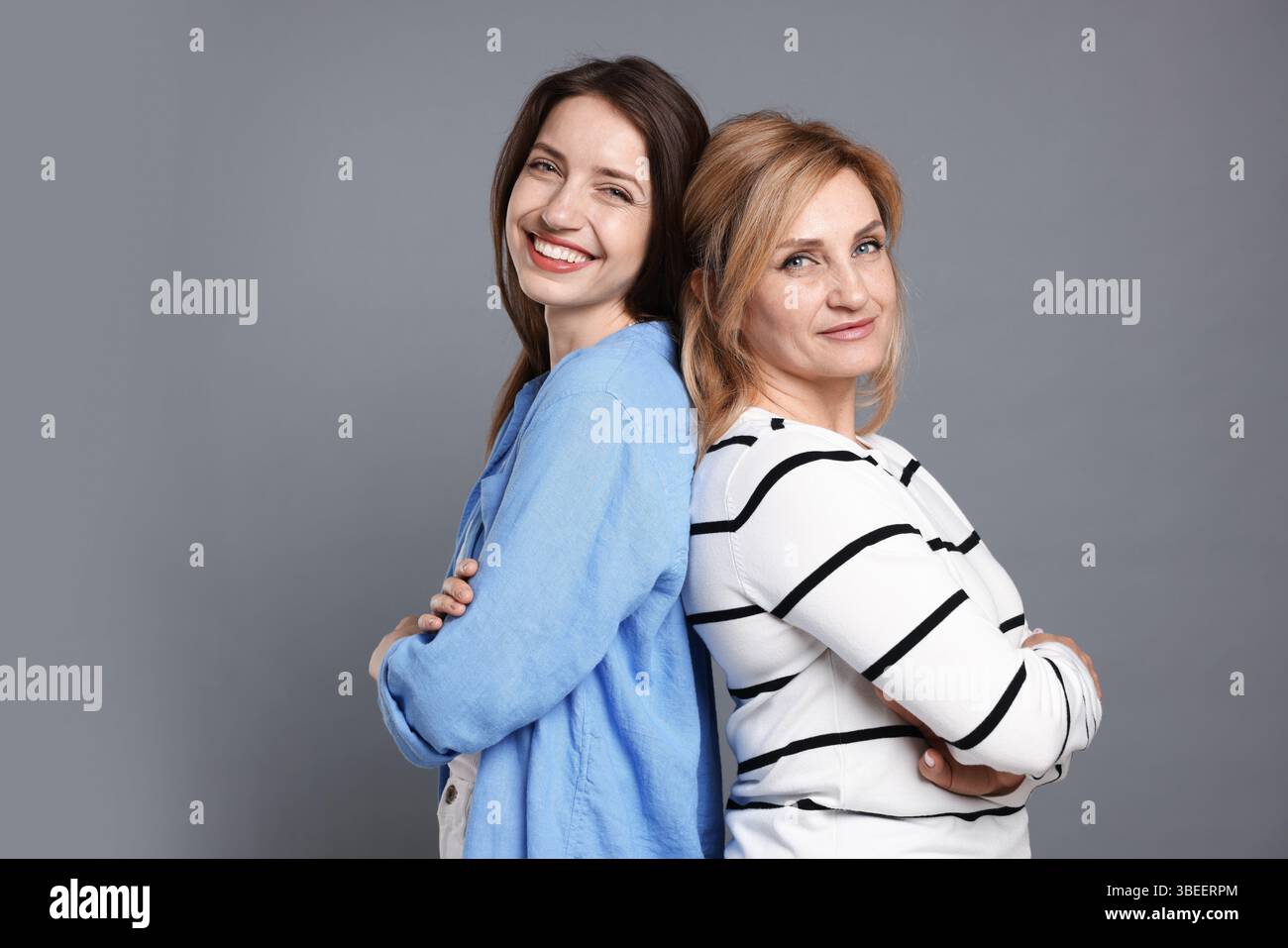 Mère et fille joyeuses dos à dos sur fond gris Banque D'Images