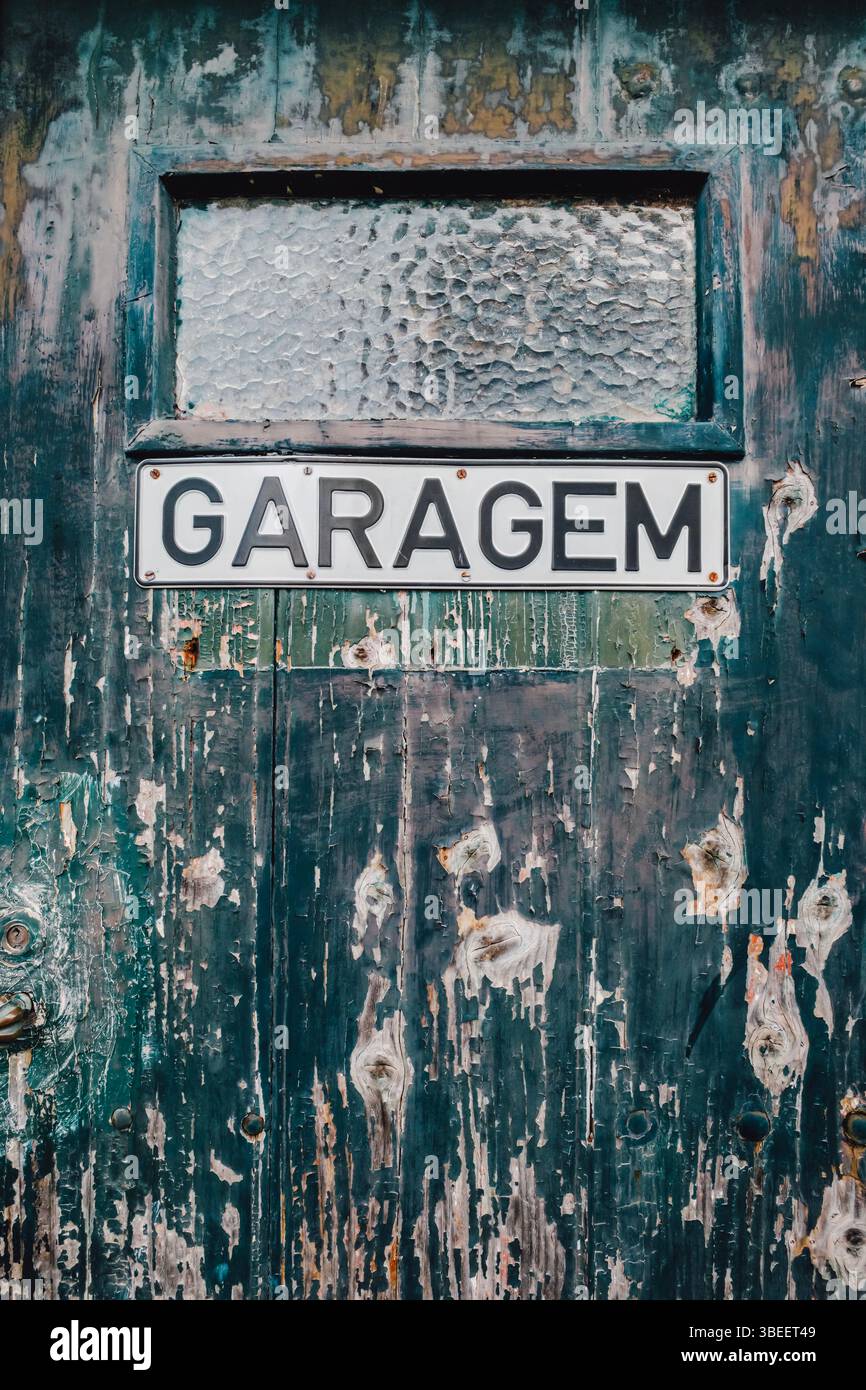 Porte de garage vintage patinée avec peinture verte pelable affiche le signe portugais Garagem sur la surface en bois vieilli. Spectacle d'architecture côtière rustique Banque D'Images