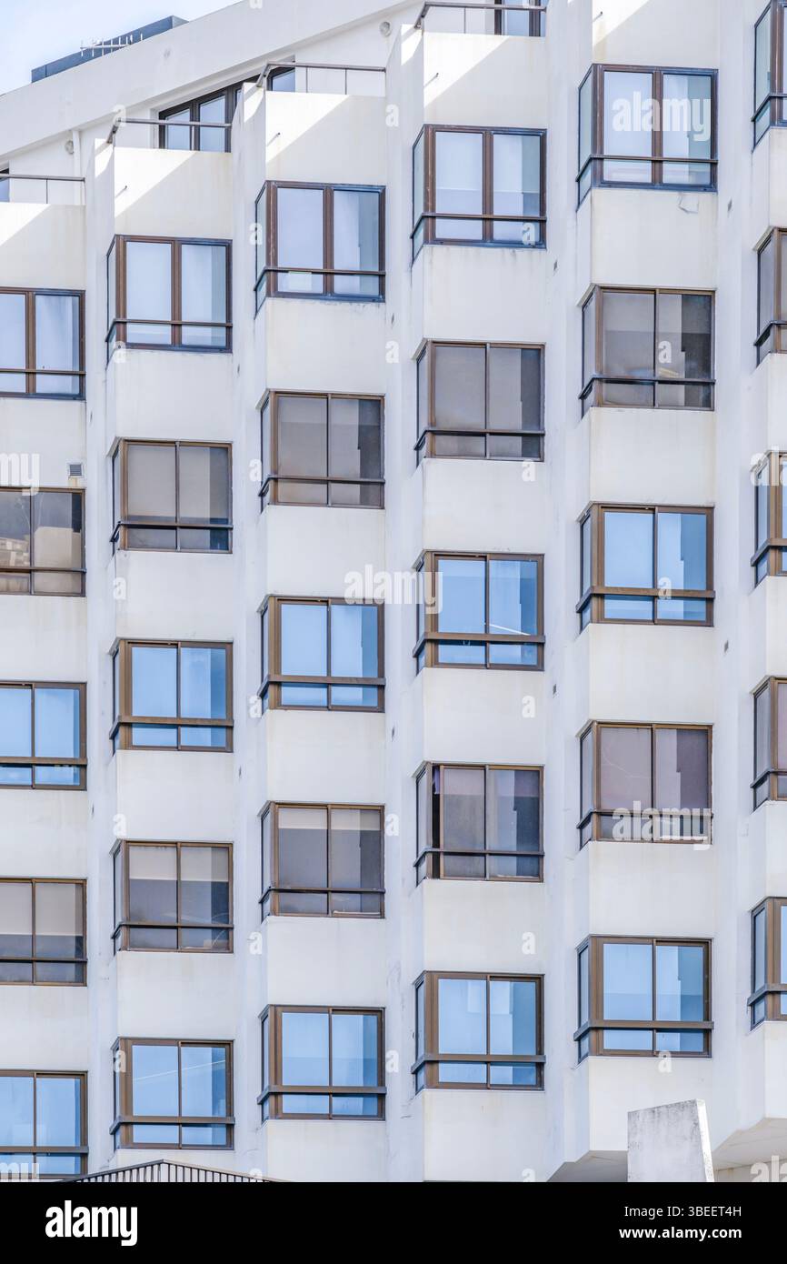 La façade blanche moderne de l'immeuble d'appartements présente un motif géométrique de fenêtres et de balcons dans une architecture résidentielle contemporaine. Design épuré et minimaliste Banque D'Images