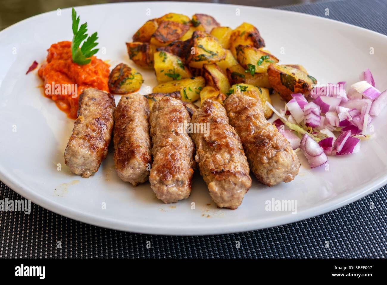 Cevapcici traditionnel (saucisses) avec pommes de terre rôties et oignons frais. Croatie Banque D'Images