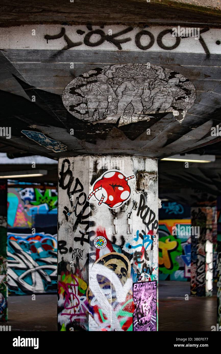 Des graffitis colorés recouvrent des piliers en béton dans une zone urbaine de Londres. L'art comprend divers dessins et éléments d'art de rue. Banque D'Images