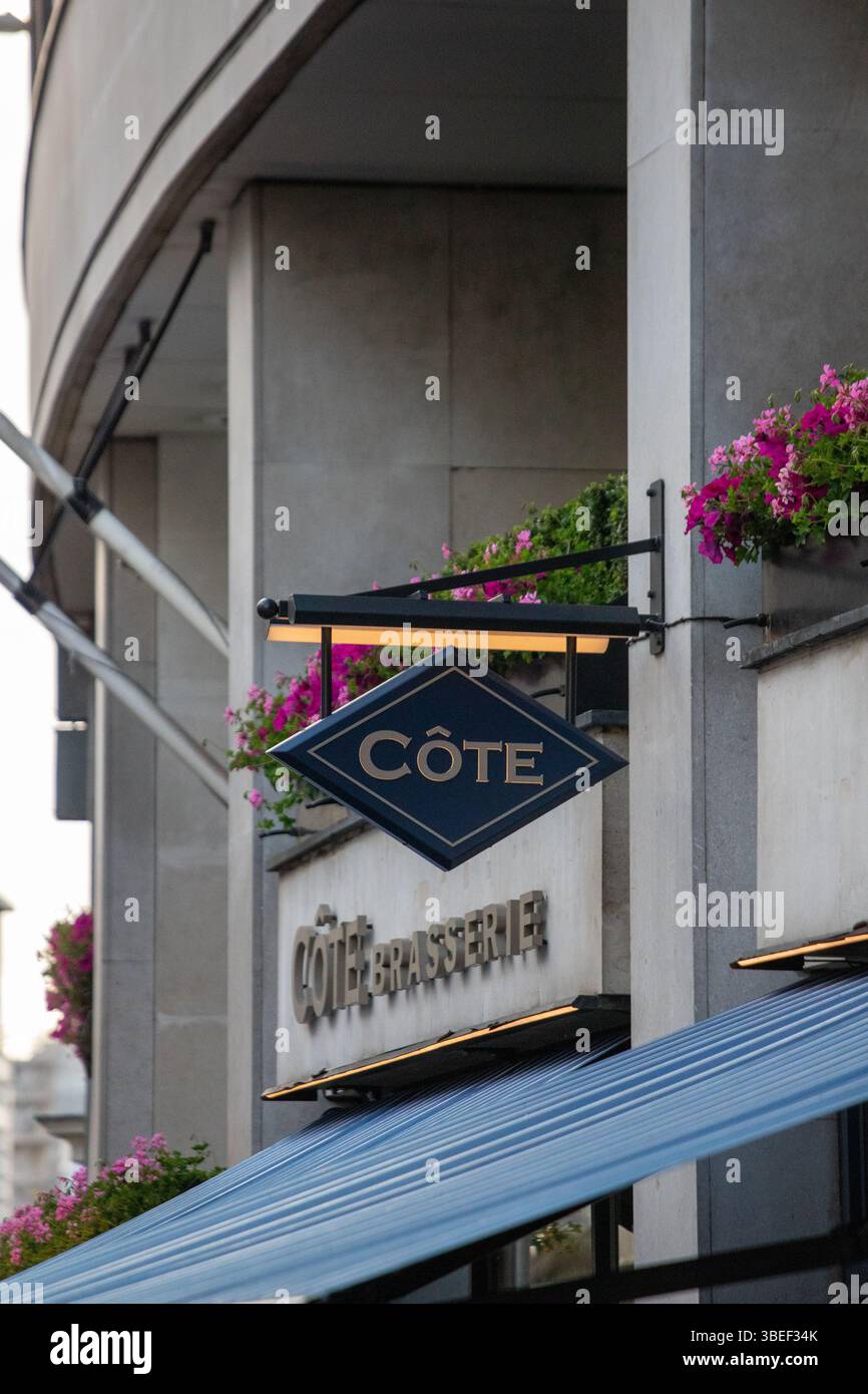 Un panneau pour Cote Brasserie accompagné de fleurs colorées à Londres. Le cadre urbain ajoute du charme à la façade des restaurants. Banque D'Images
