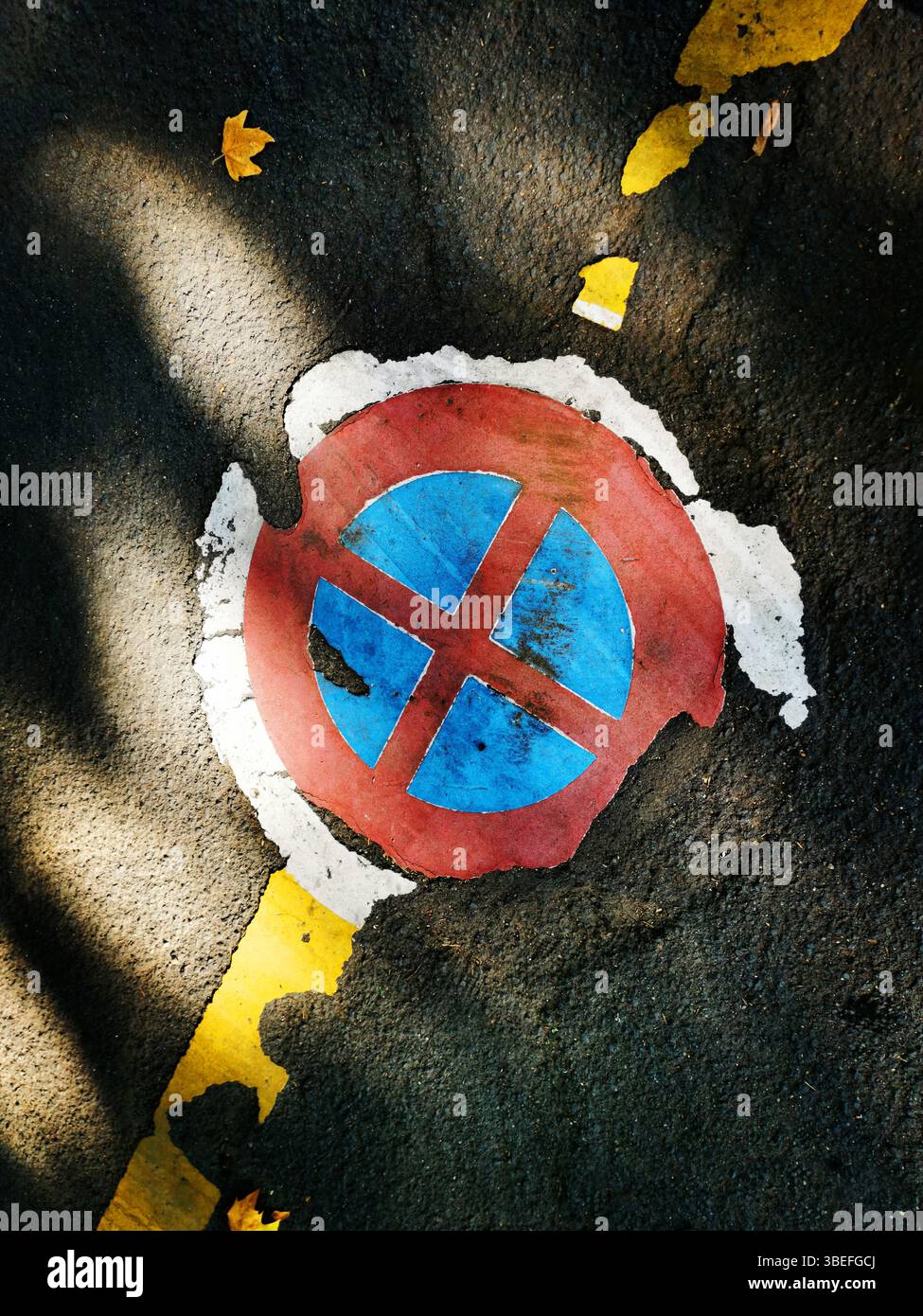 Un symbole de stationnement circulaire de couleurs rouge et bleue apparaît usé et fissuré sur une surface asphaltée. Des lignes jaunes bordent le panneau Banque D'Images