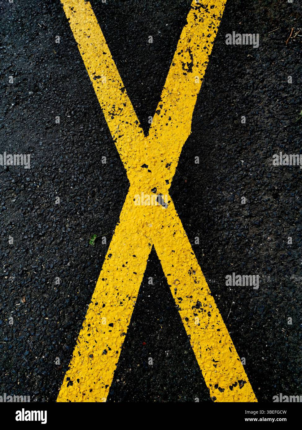 Un motif de lignes de croisement jaunes peintes sur une surface en asphalte foncé souligne un contraste visuel audacieux. Banque D'Images