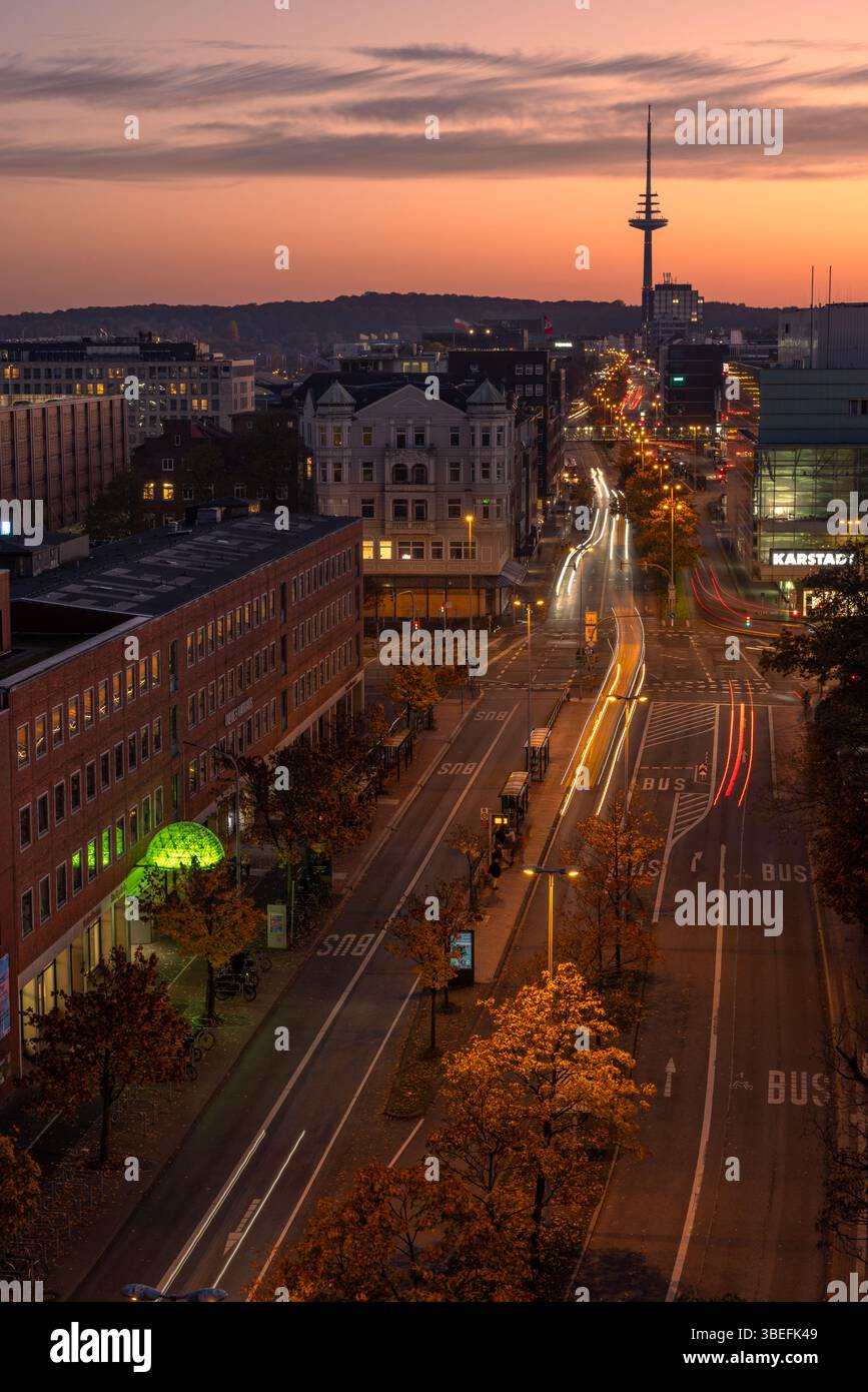 Vue longue exposition sur le centre de Kiel, en Allemagne, avec des sentiers de feux de circulation, des arbres d'automne et des bâtiments d'horizon au crépuscule. Usage éditorial exclusif. Banque D'Images