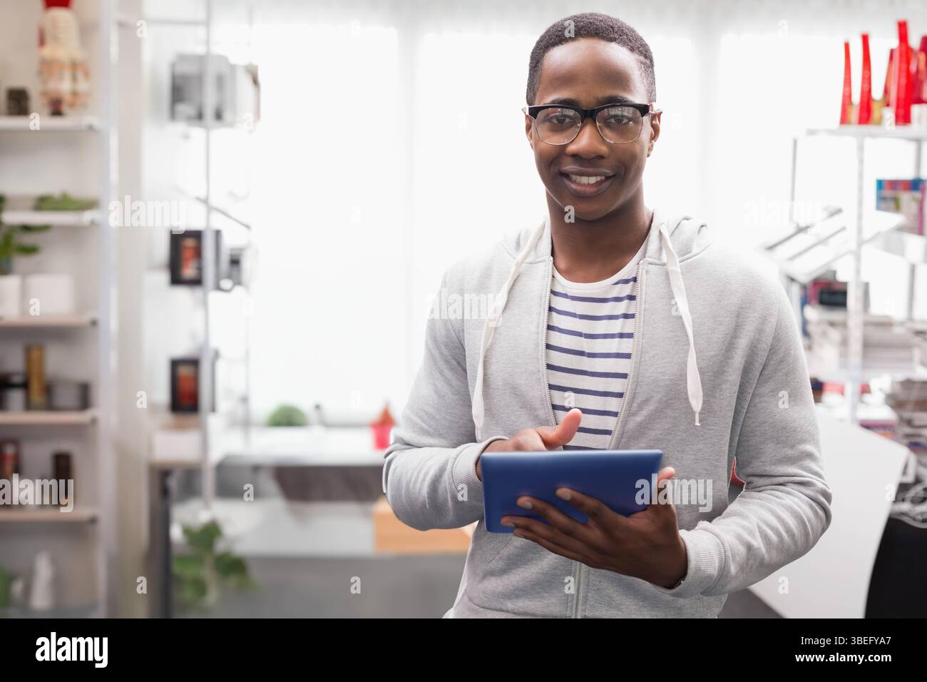 Tablette bleue assise sur le bureau par des étagères blanches avec des plantes en pot et des bouteilles rouges dans le studio Banque D'Images