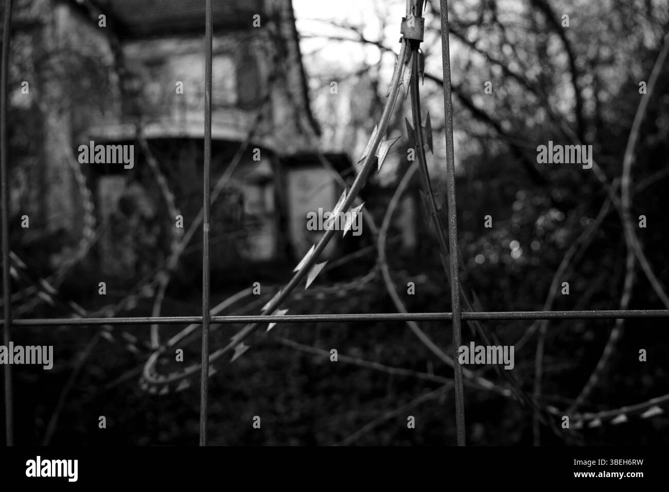 Du fil de fer barbelé entoure un bâtiment abandonné dans un endroit urbain désolé en fin d'après-midi Banque D'Images