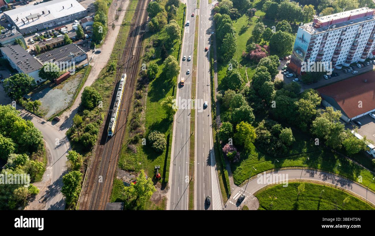 Vue aérienne verticale du corridor routier urbain vert et de la ligne de chemin de fer avec des appartements de grande hauteur, illustrant le transport urbain durable et l'intégration du logement Banque D'Images