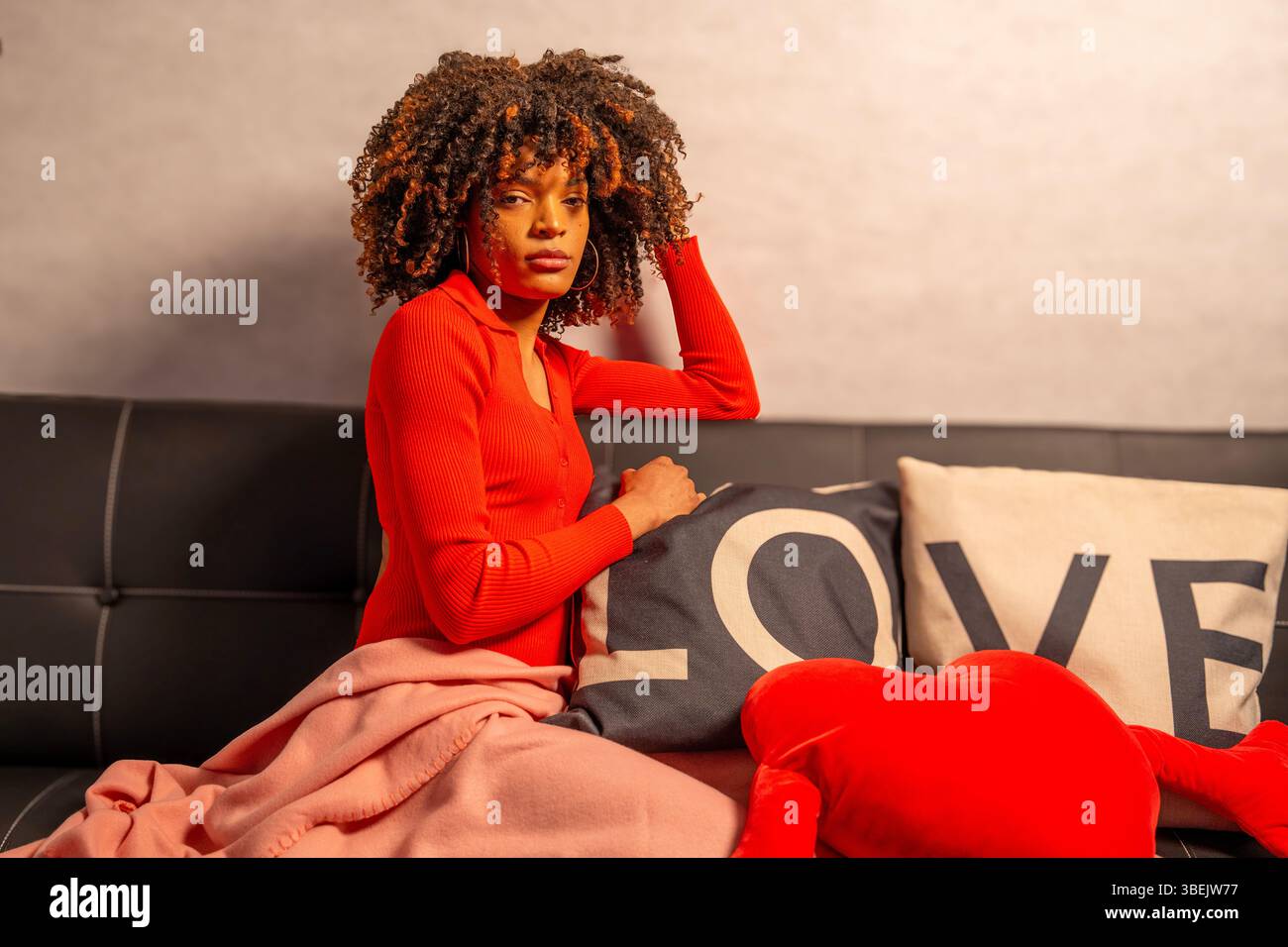 Femme élégante profitant d'un moment de détente sur un canapé confortable orné de coussins sur le thème de l'amour et d'un oreiller en forme de coeur moelleux Banque D'Images