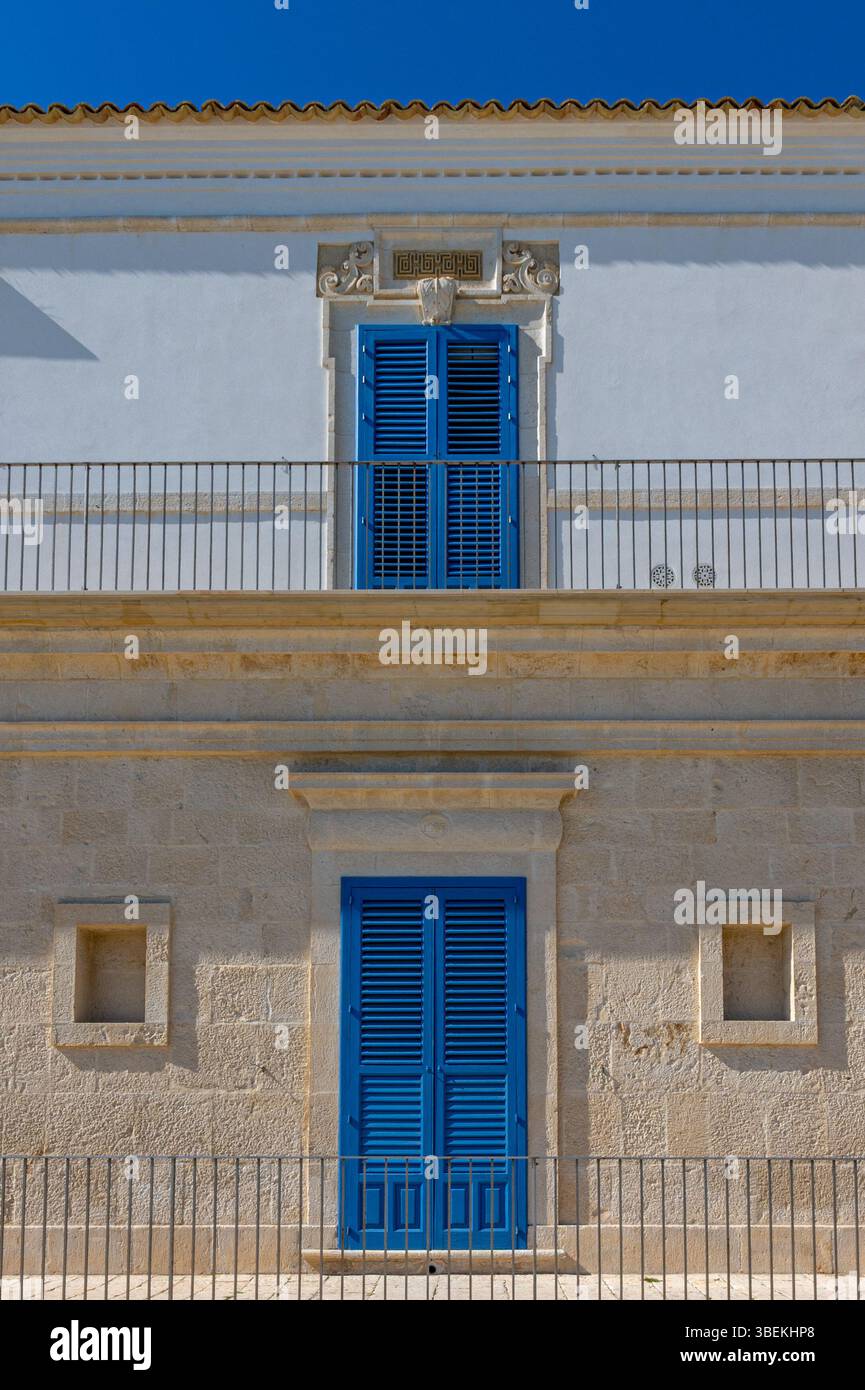 Façade en pierre et blanc rugueux avec volets bleus d'une maison située en Sicile, Italie, prise sur une journée d'hiver ensoleillée sans personne. Banque D'Images