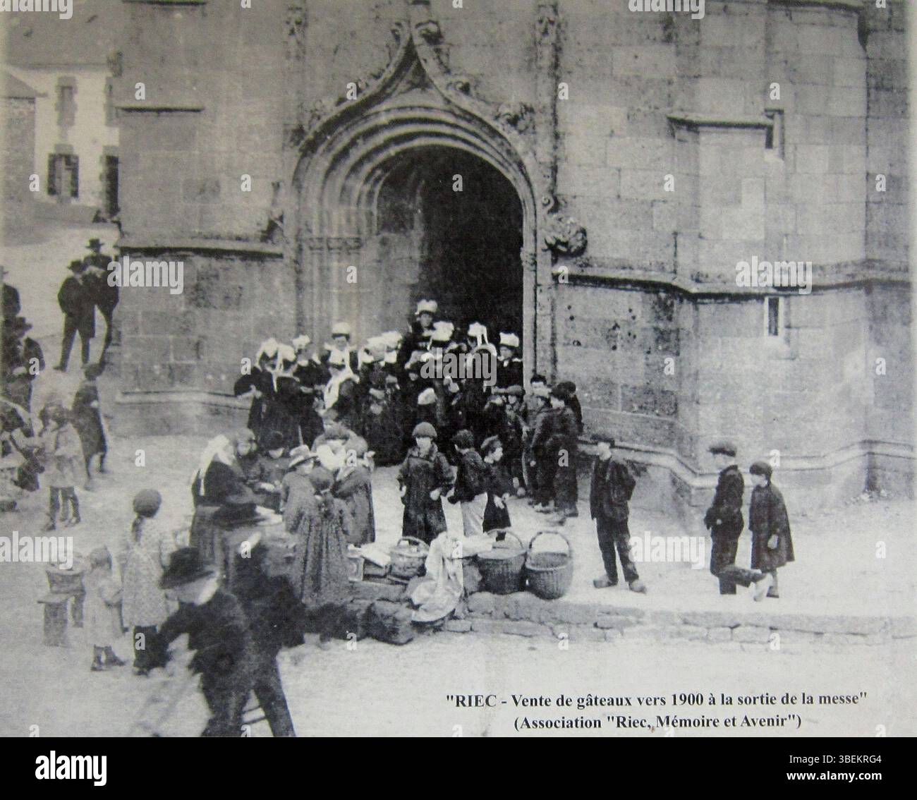 Cette image capture l'église paroissiale Saint-Pierre à Riec-sur-Bélon, France, montrant un événement traditionnel datant d'environ 1900. La carte postale, rééditée en 2021, représente une vente de gâteaux à l'extérieur de l'église après la messe, reflétant la culture communautaire et les activités typiques de la vie villageoise française. Banque D'Images Cette image capture l'église paroissiale Saint-Pierre à Riec-sur-Bélon, France, montrant un événement traditionnel datant d'environ 1900. La carte postale, rééditée en 2021, représente une vente de gâteaux à l'extérieur de l'église après la messe, reflétant la culture communautaire et les activités typiques de la vie villageoise française. Banque D'Images
