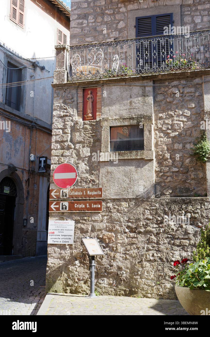 Bâtiment historique en pierre avec panneaux de signalisation à l'extérieur et sculpture pittoresque dans le mur à Montefiascone, région du Latium, Italie. 29 mai 2025 Banque D'Images