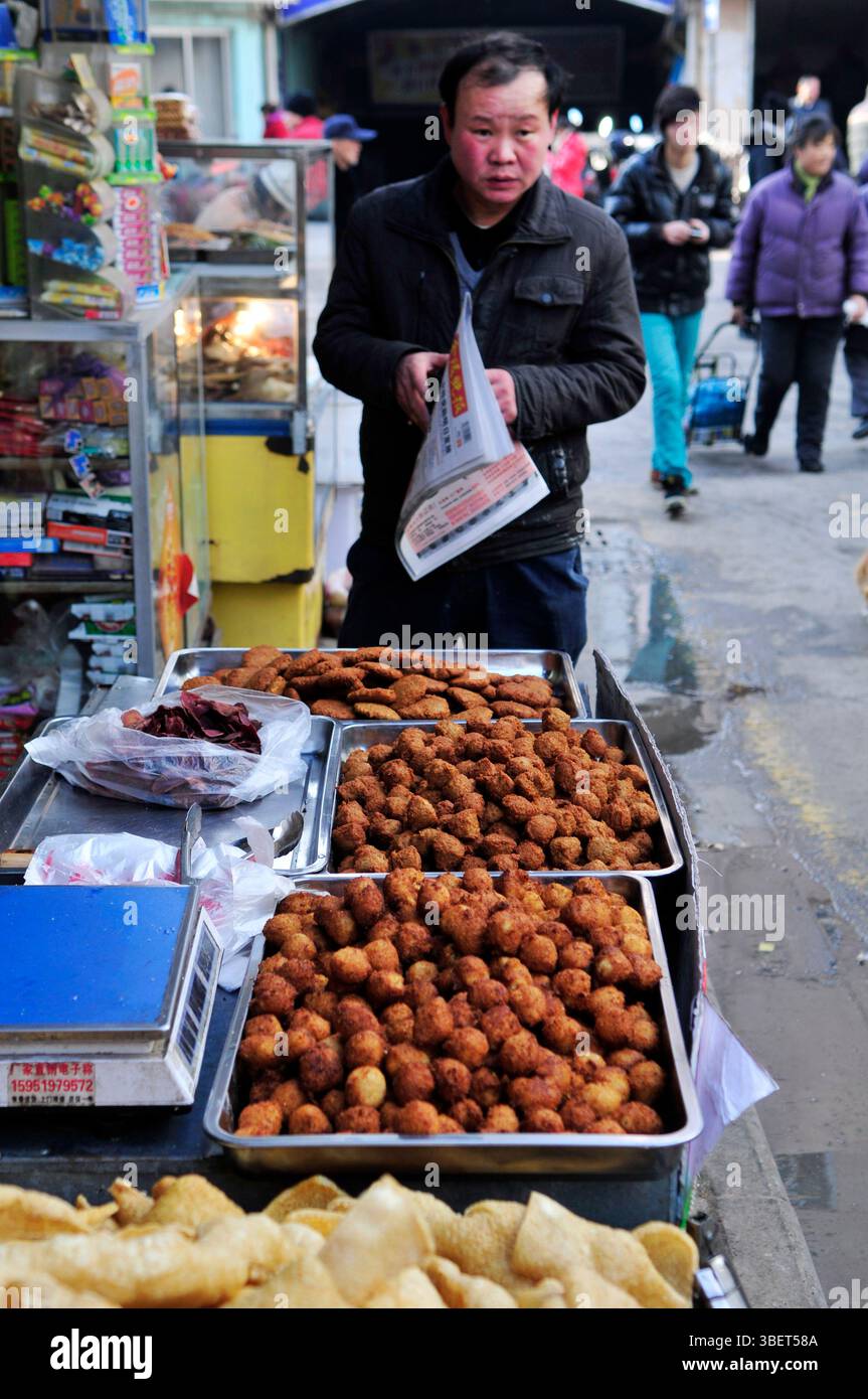 Un homme lisant le journal du matin près d'un étal de nourriture à Nanjing, en Chine. Banque D'Images