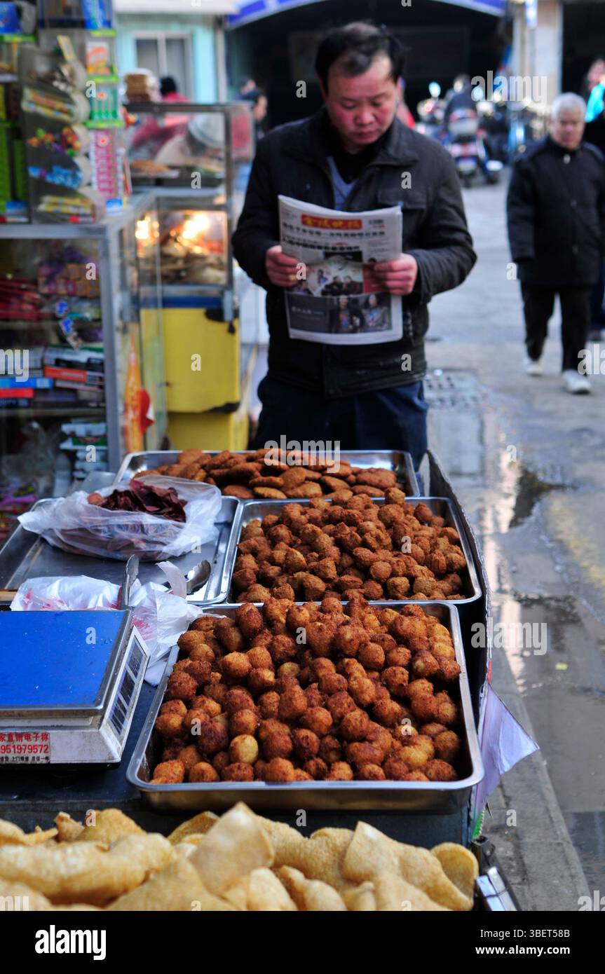 Un homme lisant le journal du matin près d'un étal de nourriture à Nanjing, en Chine. Banque D'Images