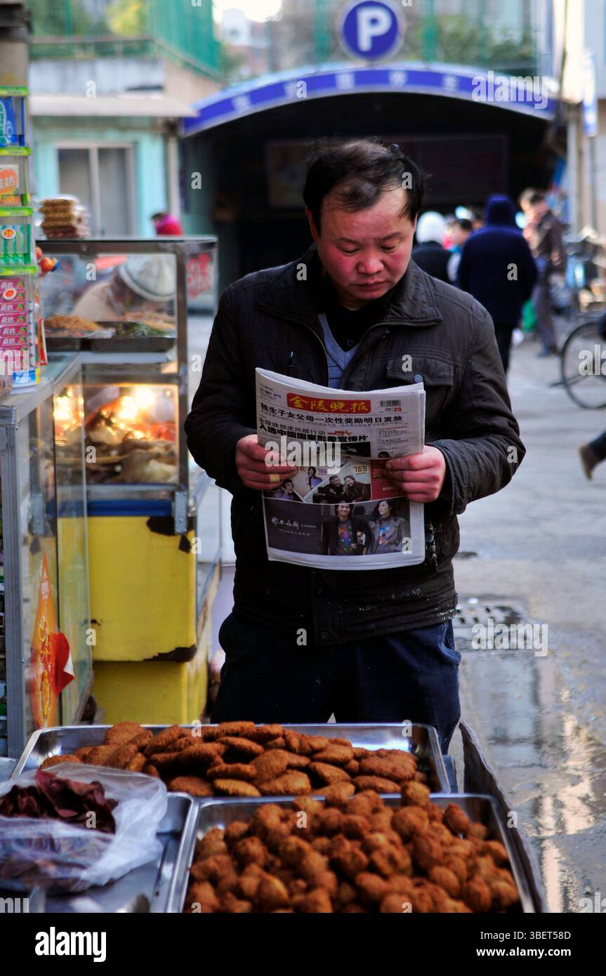 Un homme lisant le journal du matin près d'un étal de nourriture à Nanjing, en Chine. Banque D'Images
