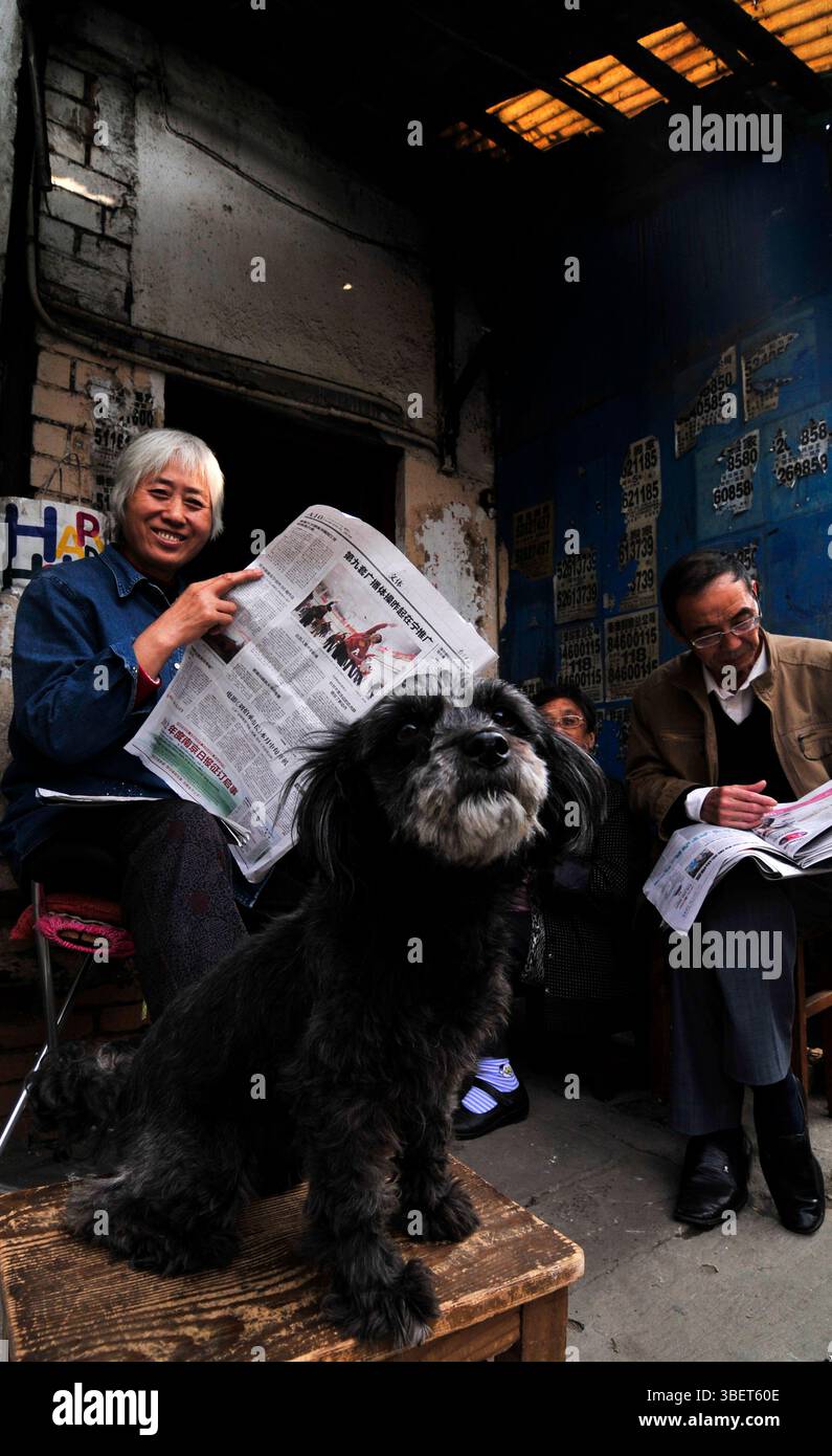 Les habitants lisent le journal du matin devant leur maison dans une petite rue de Nanjing, en Chine. Banque D'Images