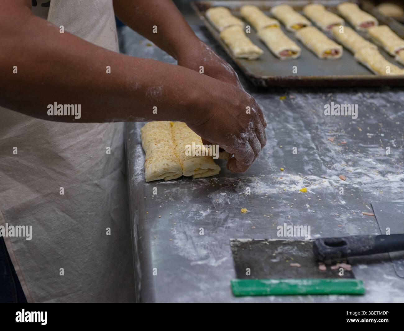 Les mains d'un boulanger façonnent soigneusement des pâtisseries garnies de graines de sésame sur une surface farinée. Banque D'Images