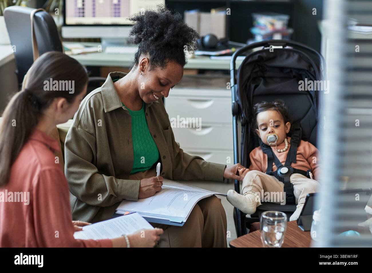 Femme d'affaires multitâche en travaillant au bureau tandis que le petit enfant est assis dans la poussette à côté d'elle dans le bureau. S'engager dans des tâches professionnelles tout en étant présent Banque D'Images