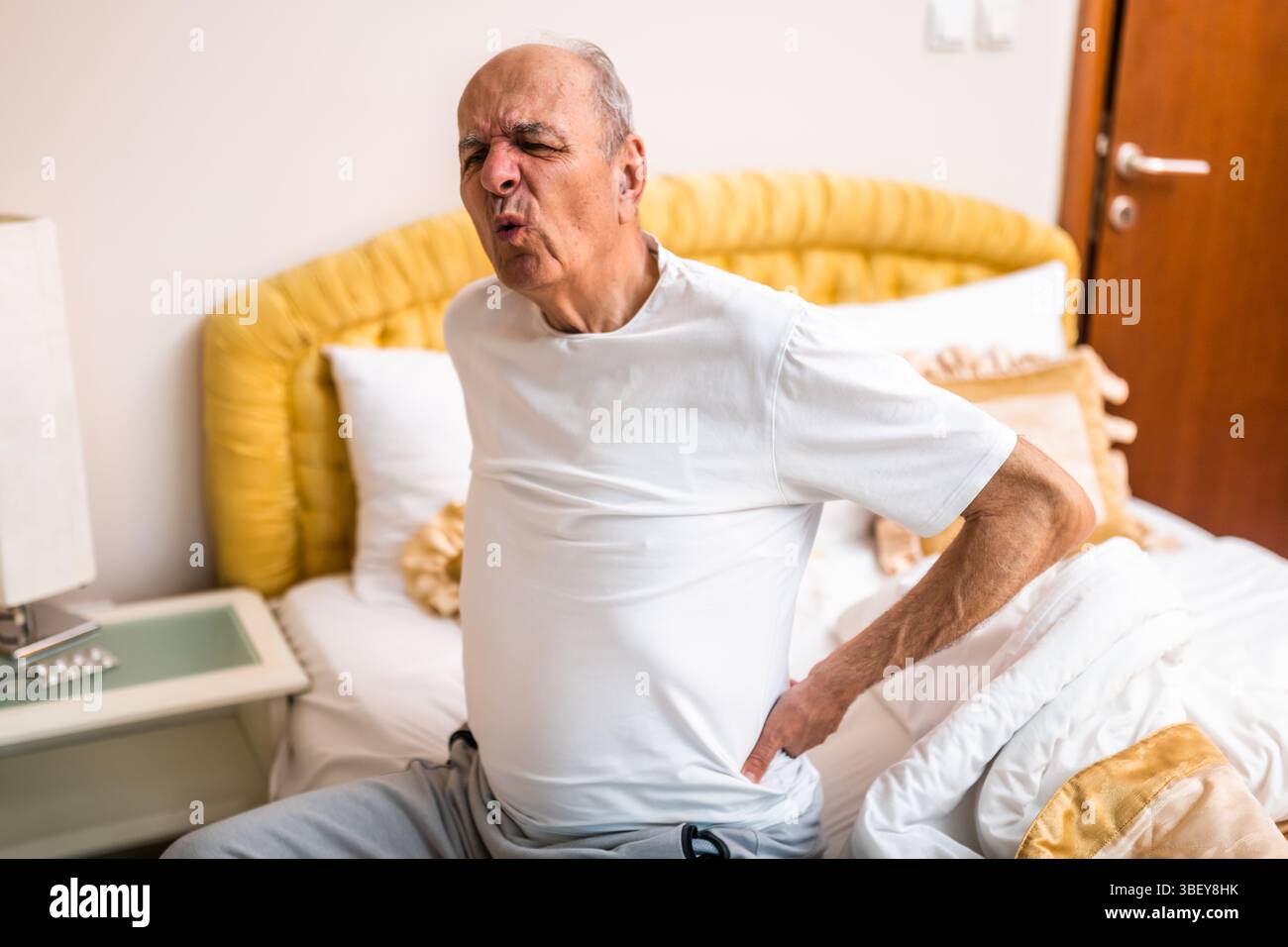 Homme âgé ayant mal au dos après s'être réveillé et assis sur le lit le matin. Banque D'Images
