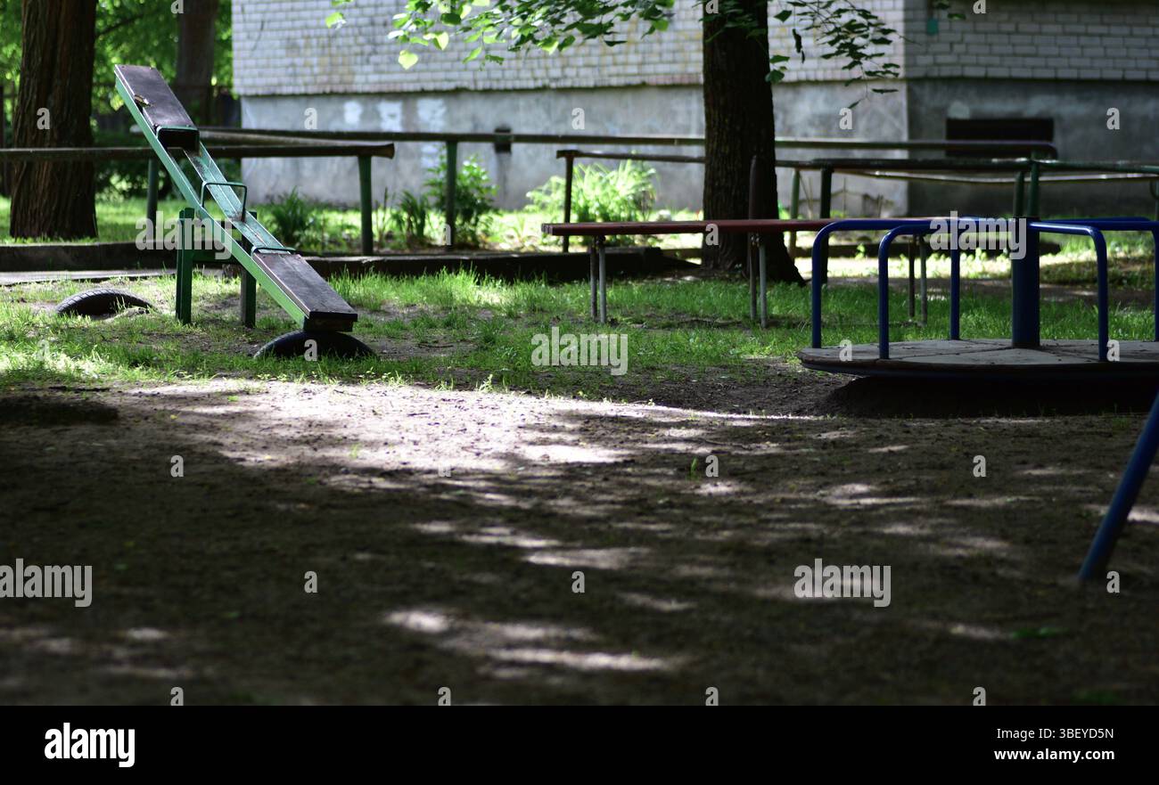 Aire de jeux abandonnée avec balançoires dispersées pour enfants et tours usés sous les arbres. La lumière tamisée, les tons de mauvaise humeur et le silence évoquent la nostalgie, l'enfance m Banque D'Images