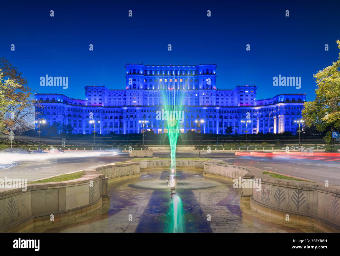 Le Palais du Parlement à Bucarest, en Roumanie, illuminé au crépuscule pendant l'heure bleue, avec des traînées de lumière de véhicule ajoutant un mouvement dynamique au A. Banque D'Images