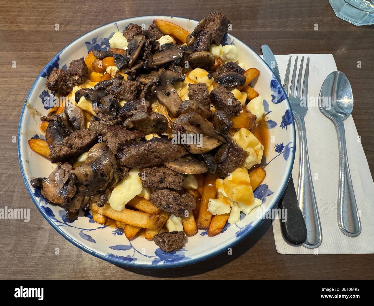 Poutine de bœuf et de champignons servie sur une table rustique dans un cadre de restaurant Banque D'Images